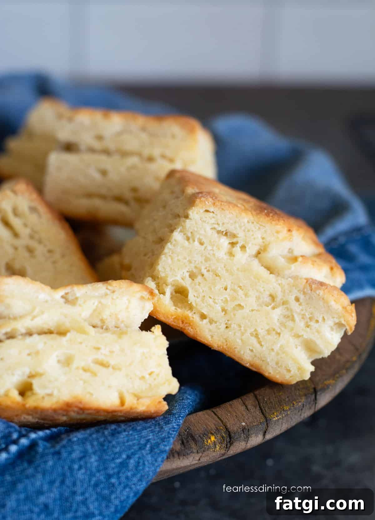 A wooden bowl with a denim napkin. The bowl is full of gluten-free sourdough discard biscuits.