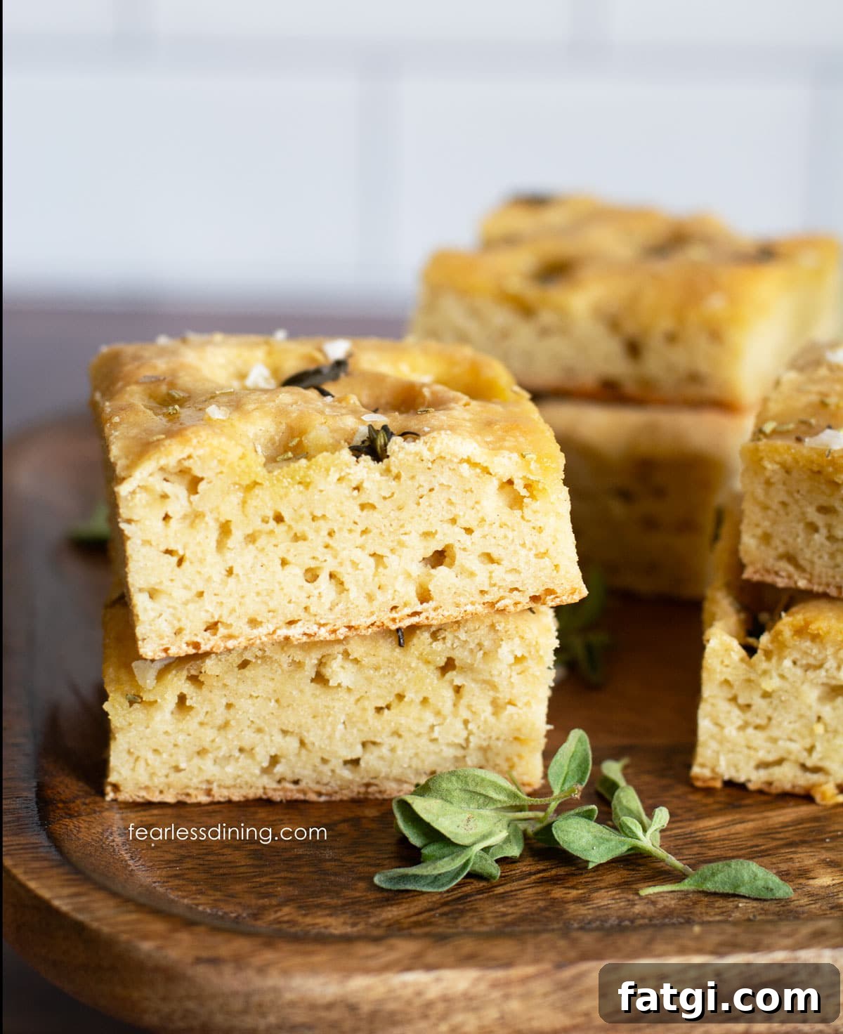 Square pieces of gluten free sourdough discard focaccia bread on a wooden cutting board.