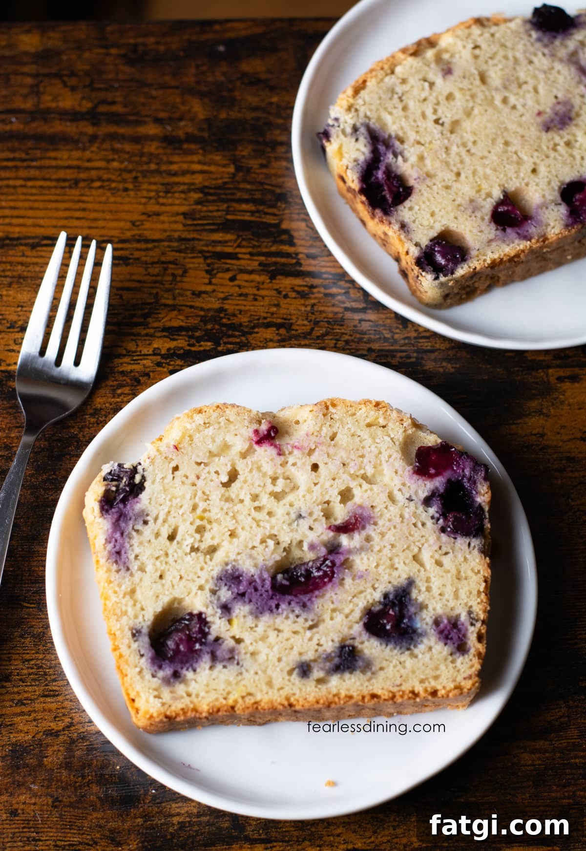 Two slices of gluten free blueberry lemon bread on small white plates.