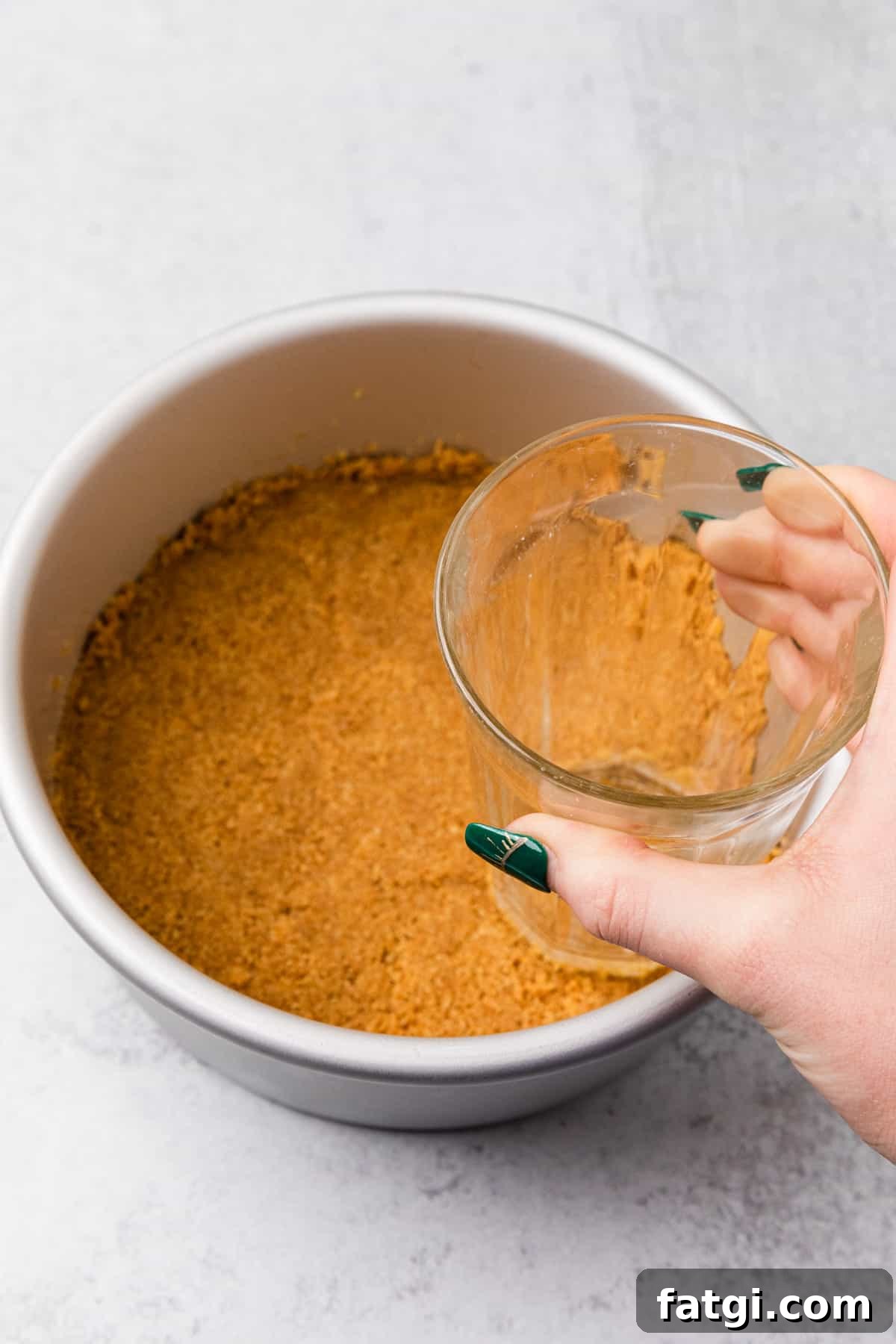 a glass pressing crumbs into a pan