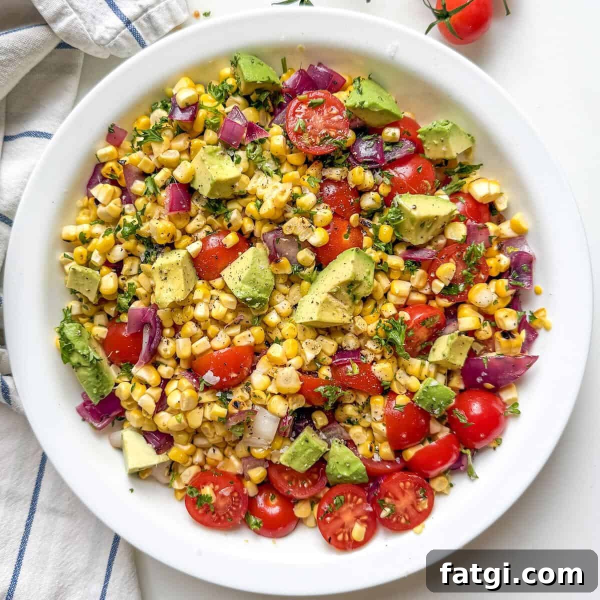 Grilled corn salad with avocado, cherry tomatoes, and lime juice served in a white bowl.