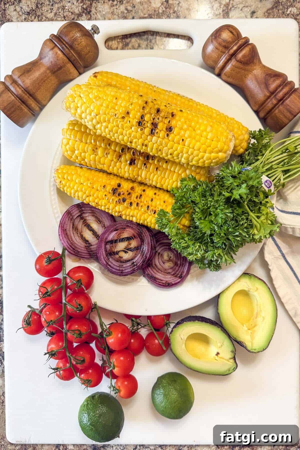 Grilled corn and onions on a platter alongside ingredients to make a corn salad.