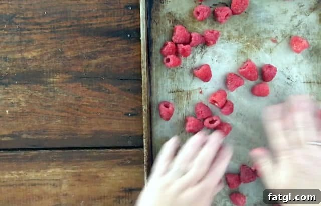 How to Freeze Raspberries for Fresh Flavor All Year 3 hand spreading out raspberries onto baking sheet