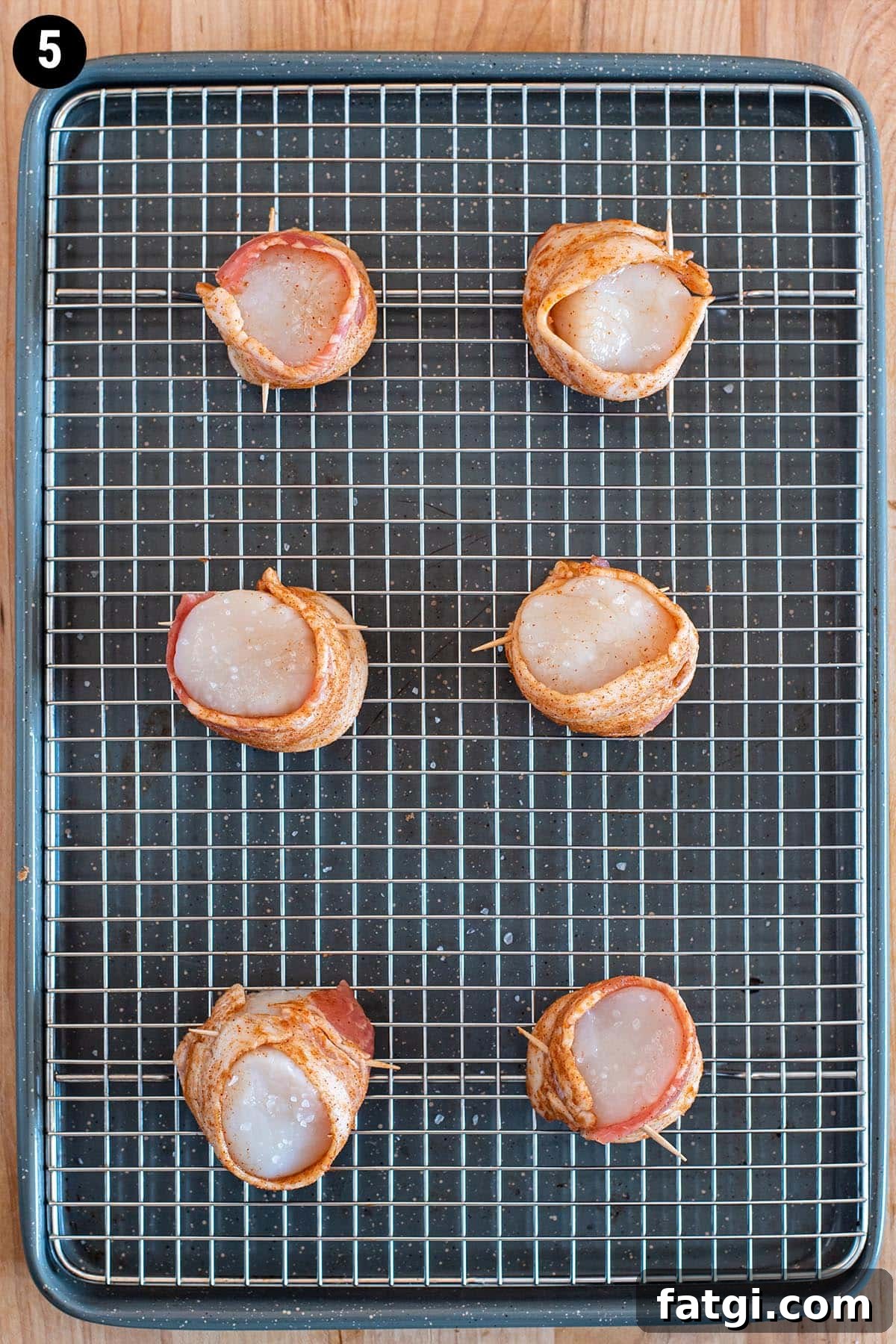 Sweet and Smoky Bacon Wrapped Scallops Recipe 8 Raw scallops wrapped in uncooked bacon on a wire rack lined backing sheet.