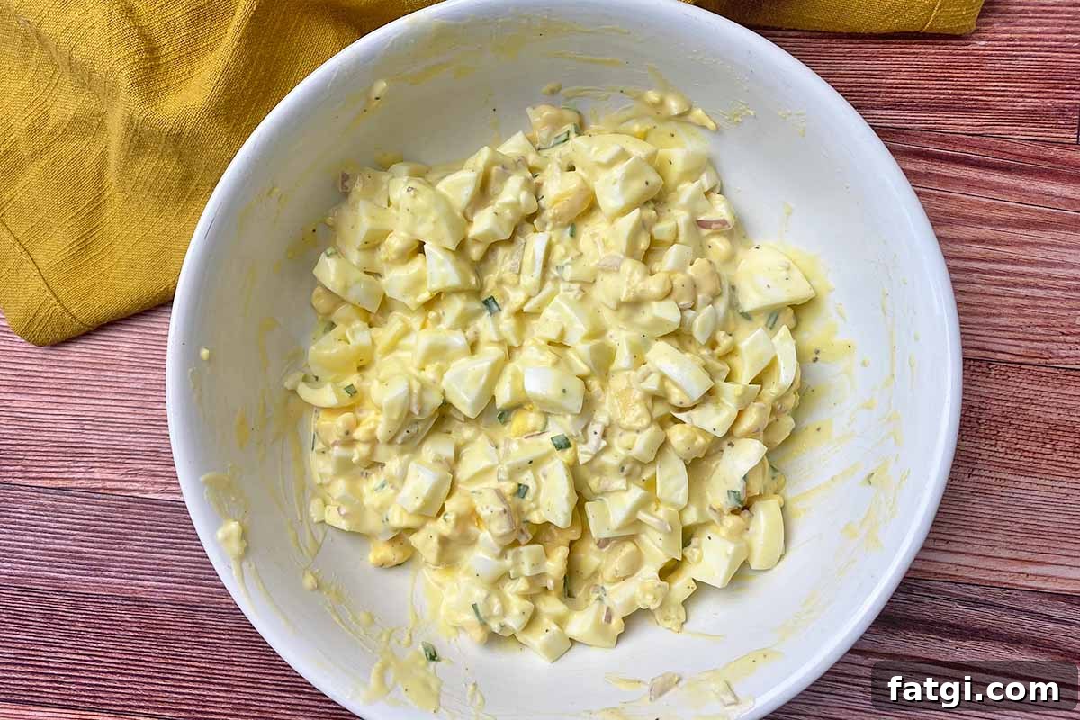 Horizontal image of a creamy, mayo-based mix with roughly chopped yolks and whites in a large white bowl.