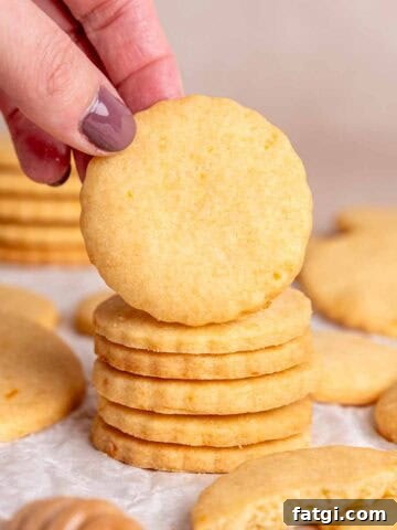 A hand grabbing an orange shortbread cookie from a stack.