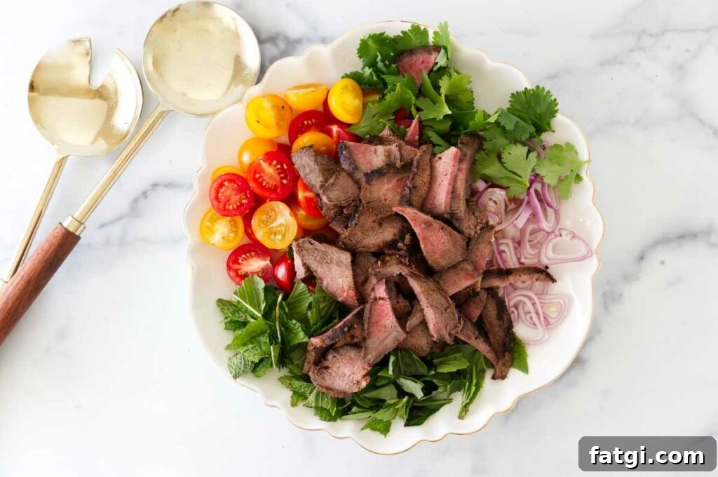 A salad plate with steak strips, fresh herbs, shallots, and tomatoes.