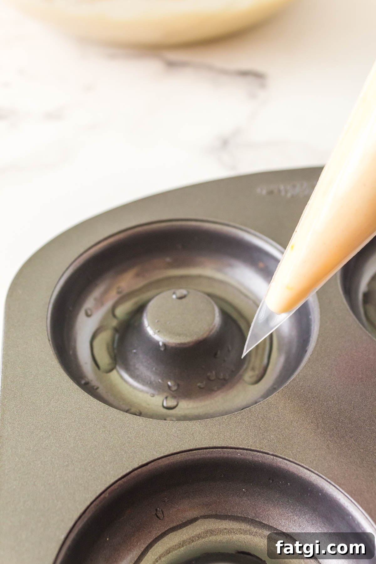 A piping bag filled with doughnut batter hovering over a doughnut pan