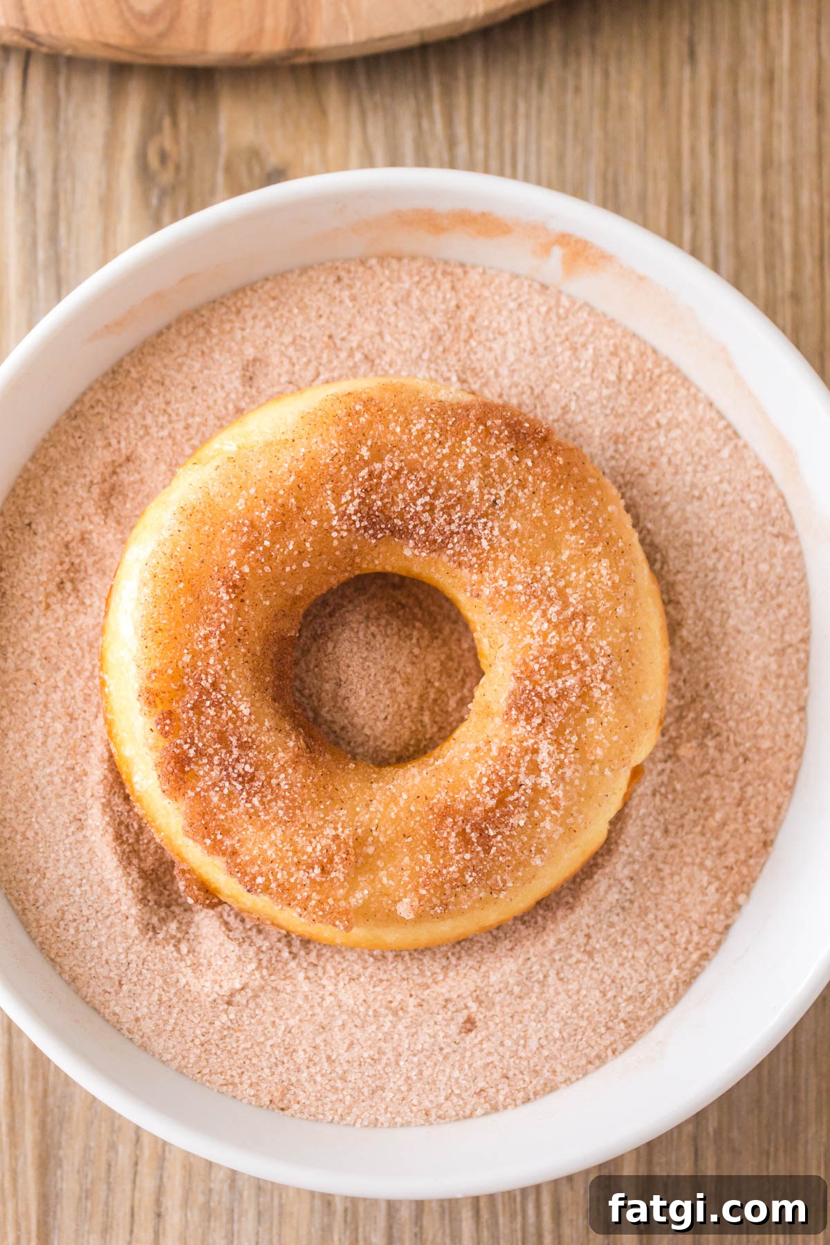 A doughnut sitting in a bowl of cinnamon and sugar mix.