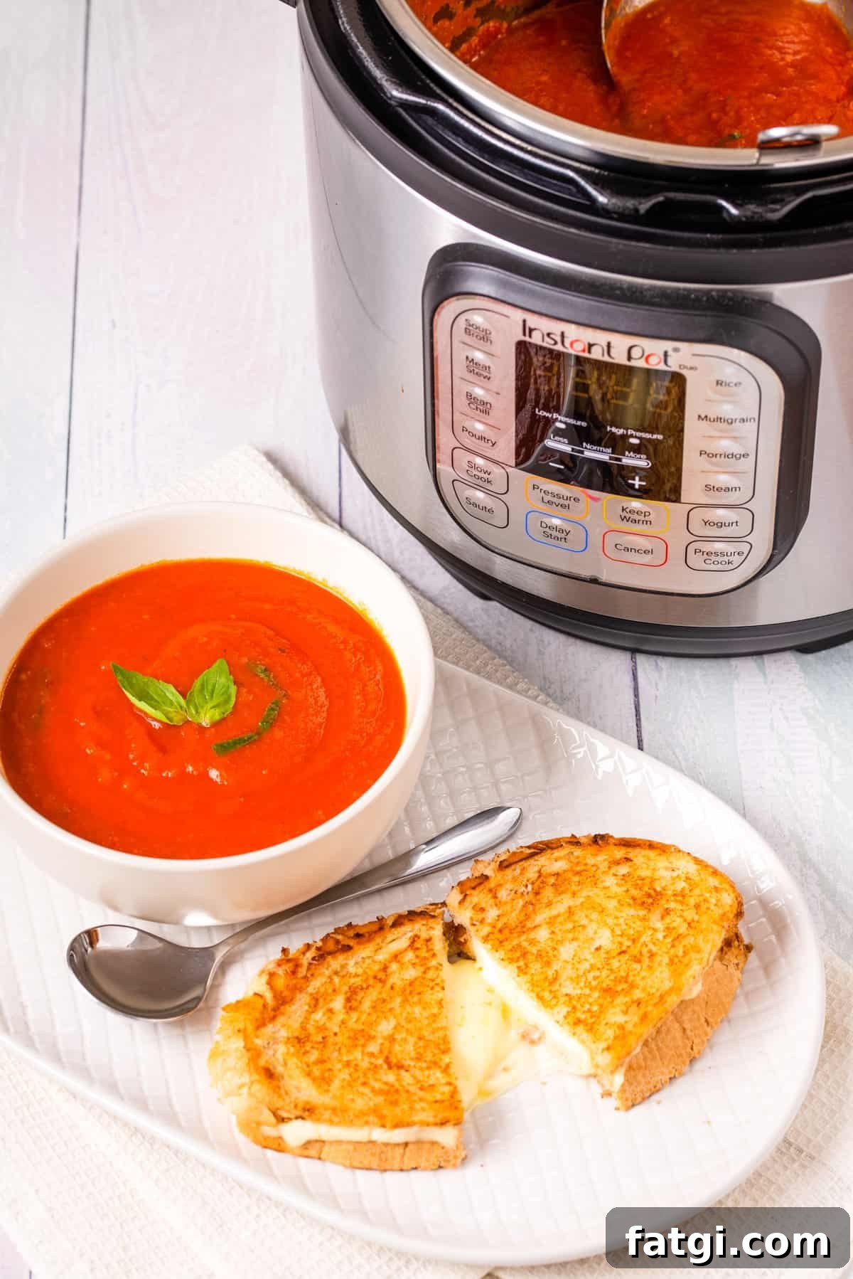 Instant Pot Tomato Soup with Fresh or Canned Tomatoes 11 Close up shot of finished tomato soup in a white bowl with a grilled cheese toastie on a white plate and instant pot in the background.