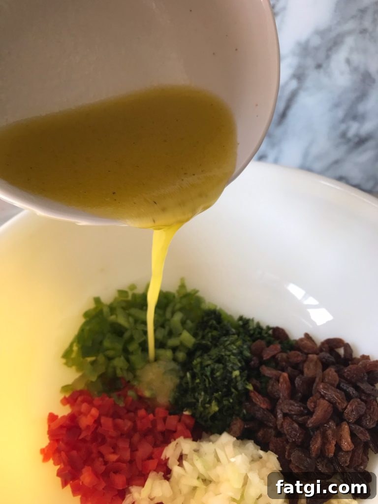 Refreshing Rose Water Quinoa Salad with Citrus & Feta 3 a freshly made lemon olive oil vinaigrette being poured into a bowl of chopped vegetables and raisins