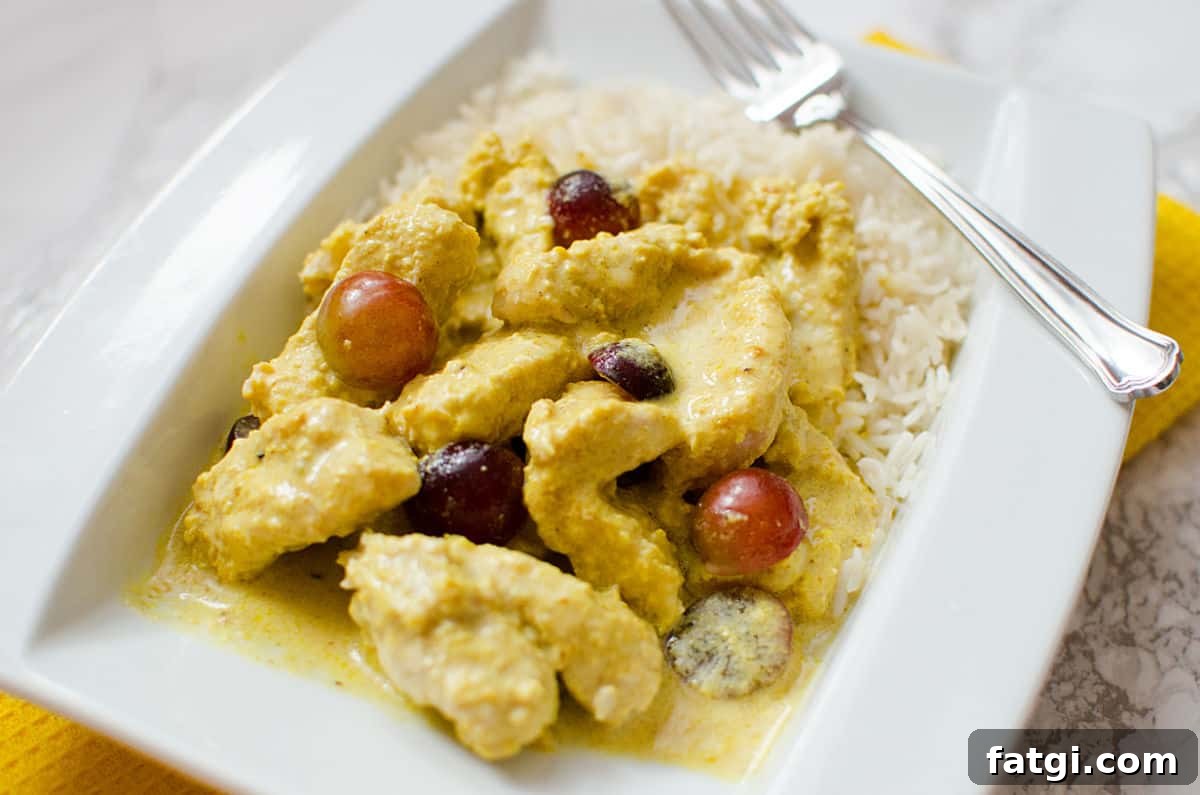 turkey curry with grapes on a white plate with a fork