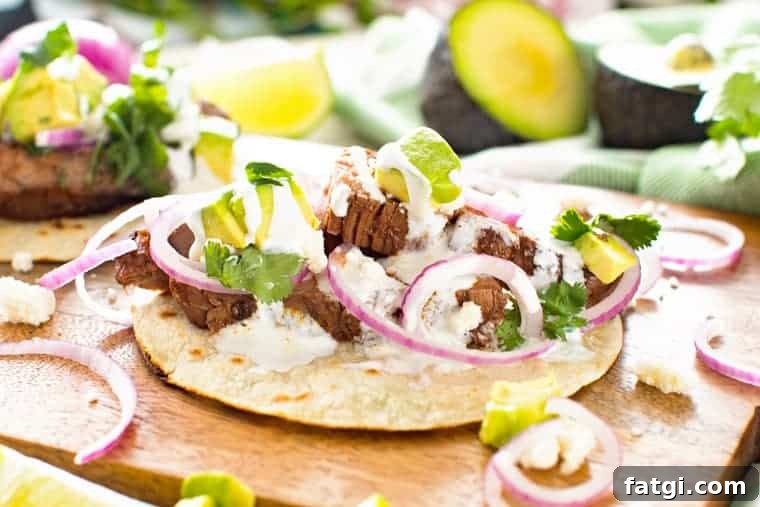 Flank steak tacos on a wooden curling board topping with cilantro, red onion and avocado.