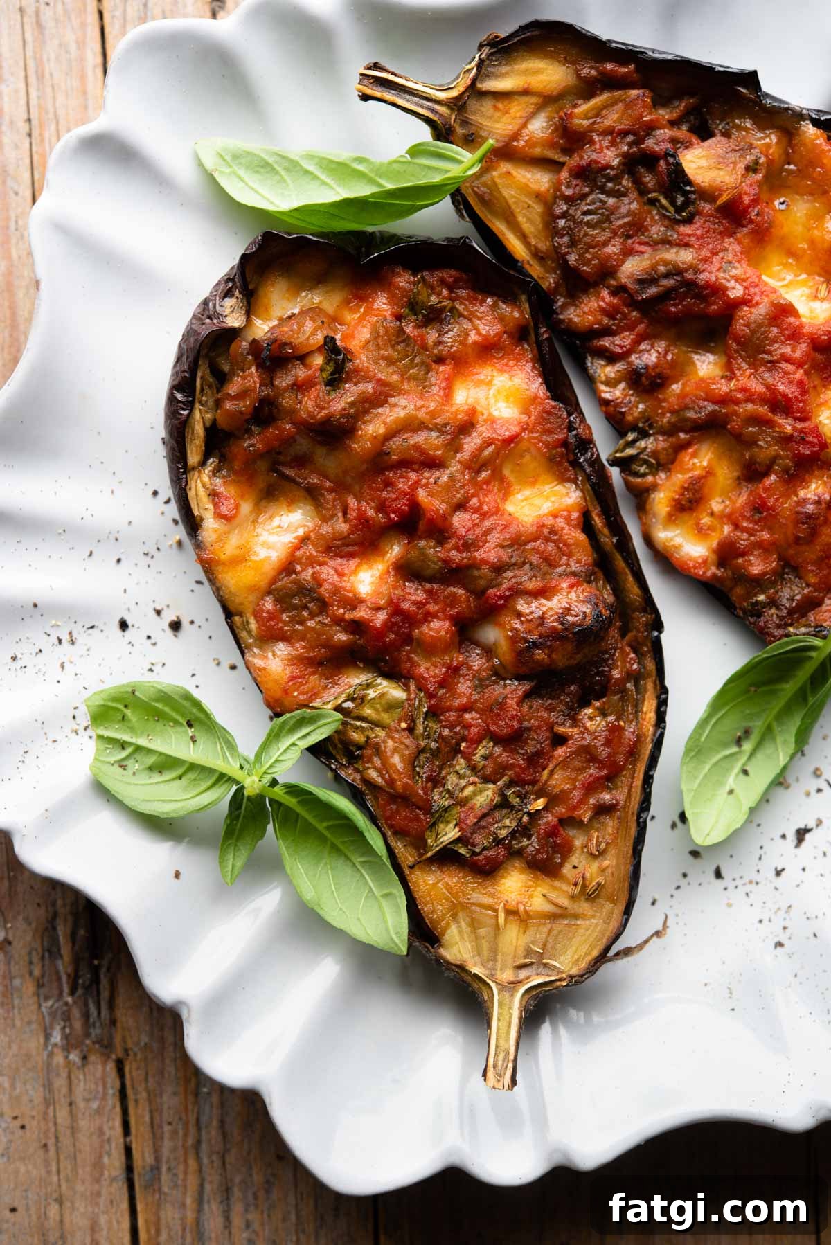 Italian Stuffed Eggplant Recipe with Mozzarella and Tomato 2 Two stuffed eggplants on a scalloped edged plate with basil scattered around.