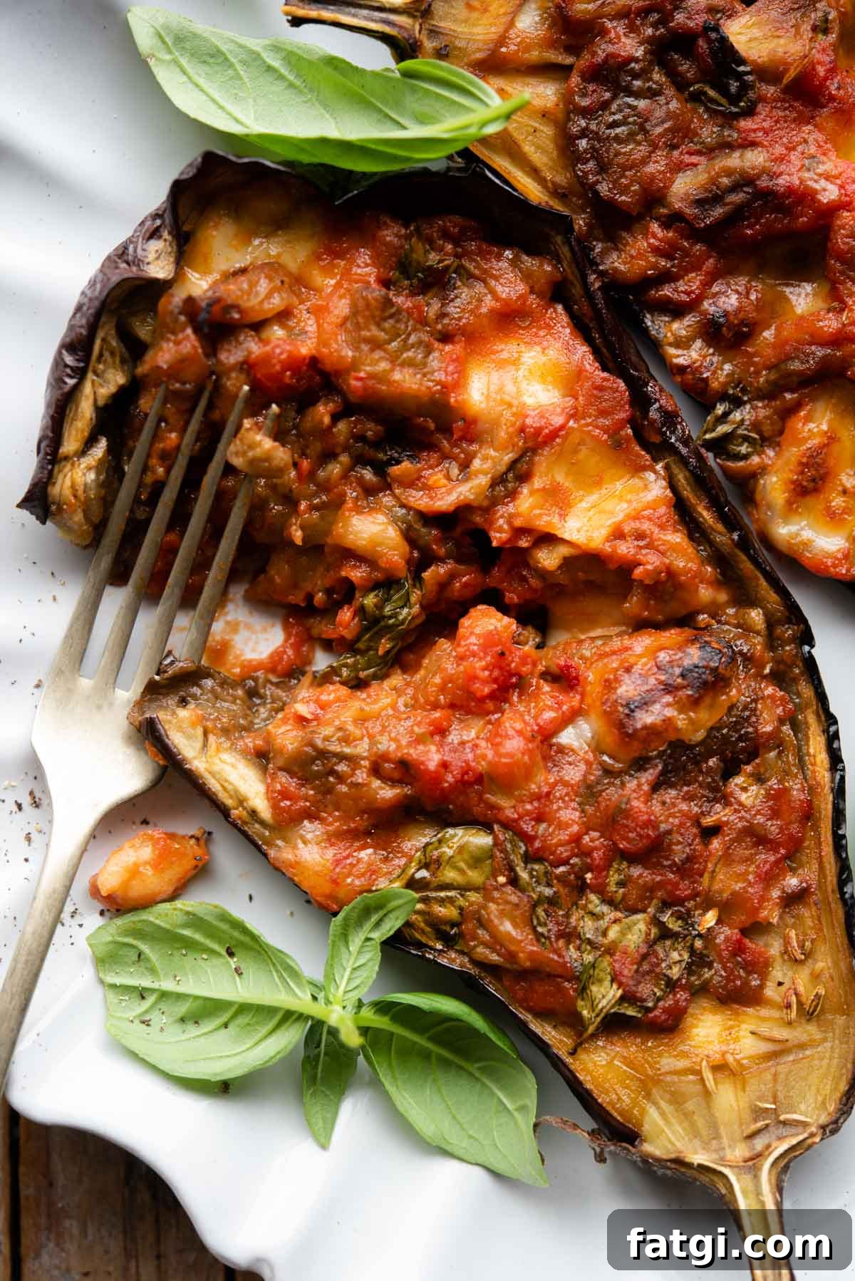 Italian Stuffed Eggplant Recipe with Mozzarella and Tomato 7 A close up of half an eggplant stuffed with tomato and mozzarella cut open on a plate.