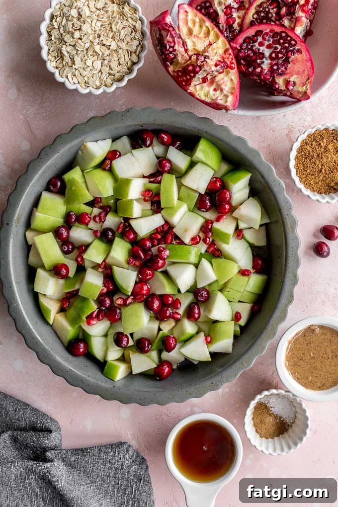 Chopped granny smith apples, cranberries and pomegranate arils mixed together in a grey pie plate.