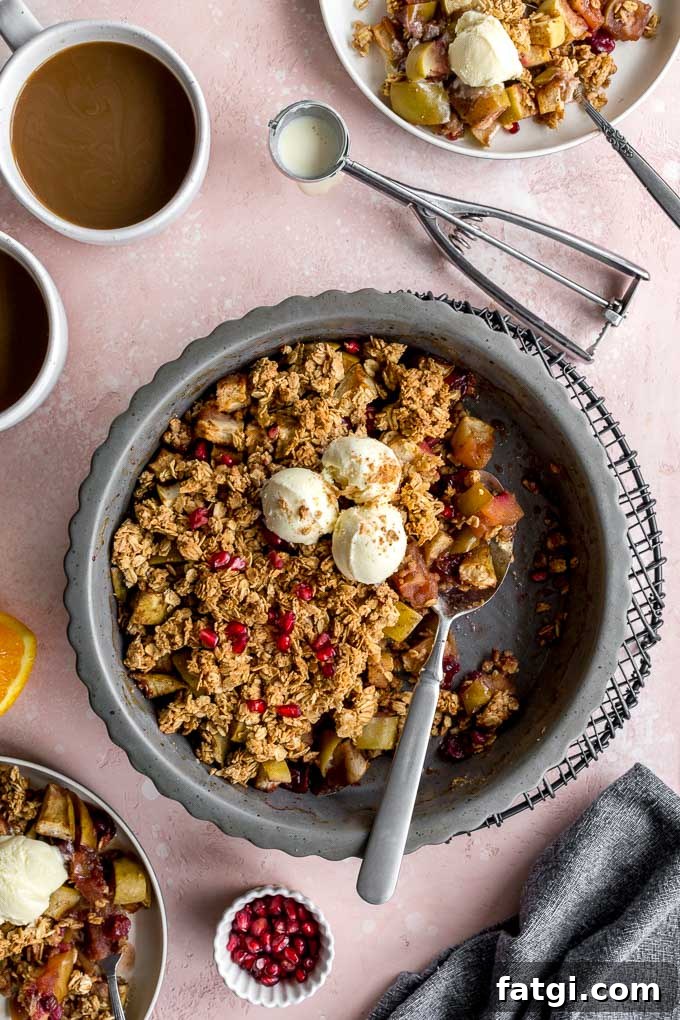 Overhead view of an apple cranberry crisp in a pie plate, topped with ice cream, and resting on a wire rack.