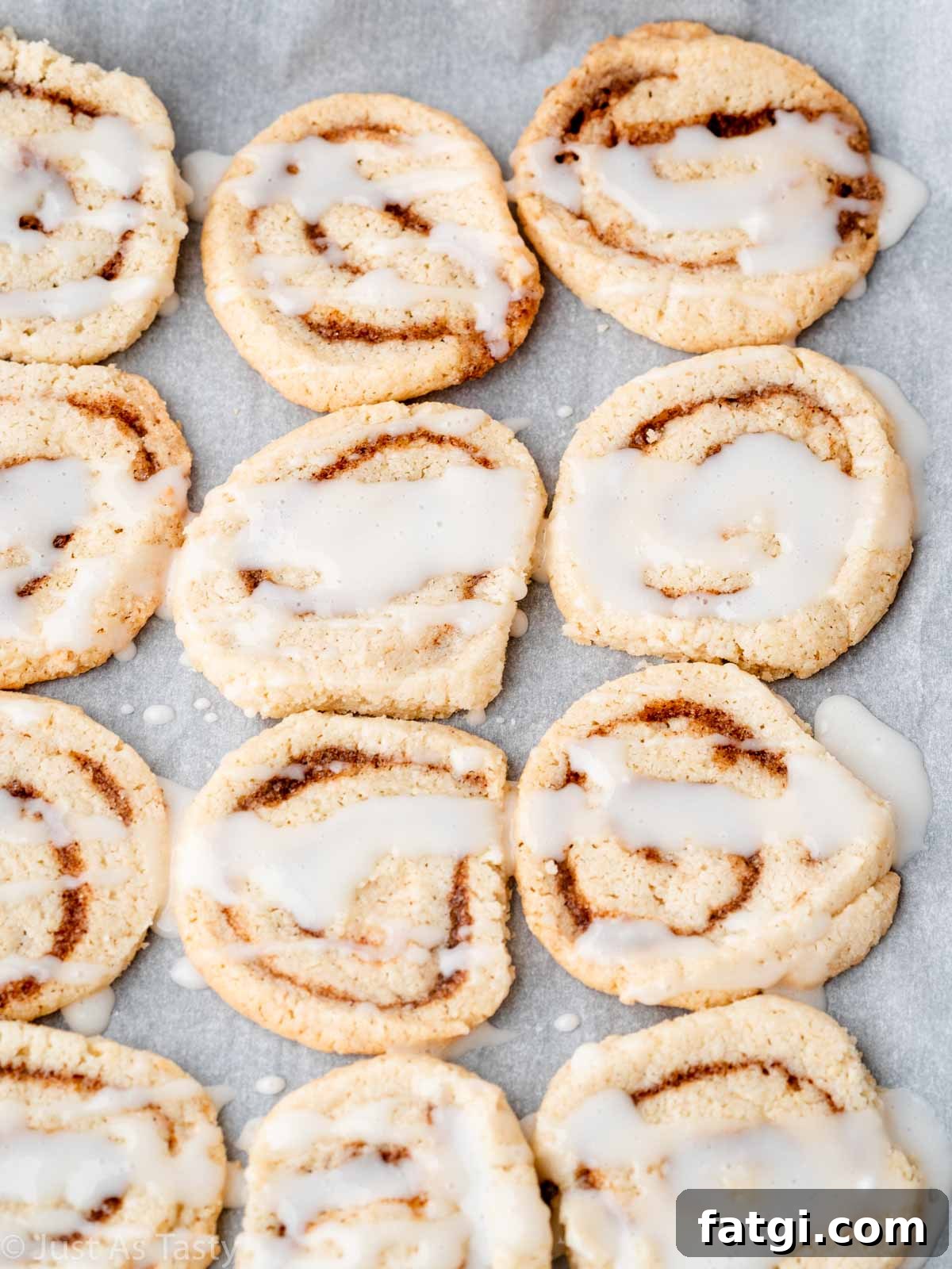 Glazed cinnamon roll cookies lined up on parchment paper. 