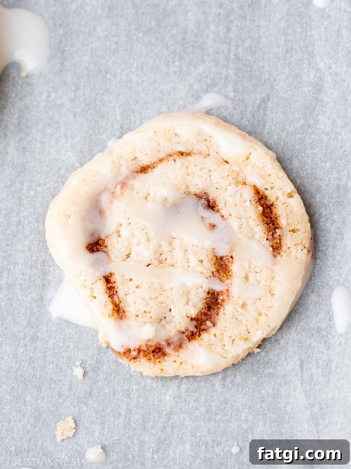 Close-up of a glazed cinnamon roll cookie on parchment paper. 