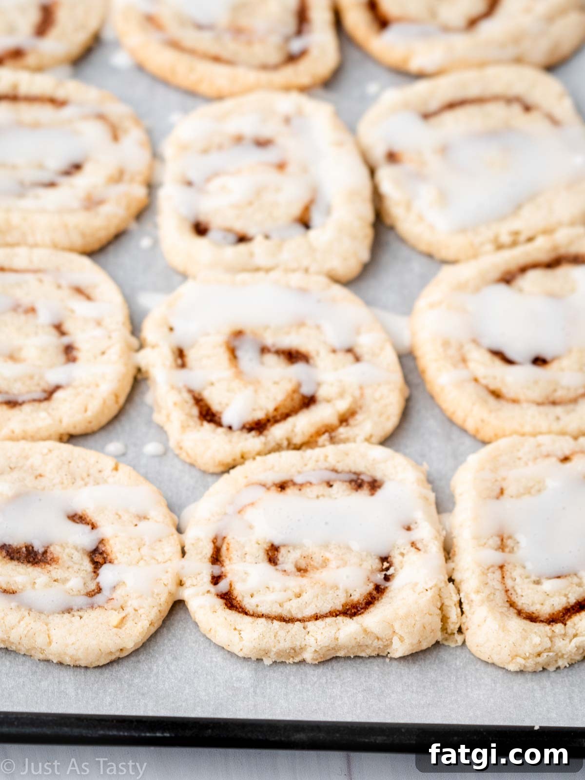 Glazed cinnamon roll cookies lined up on a lined baking sheet. 