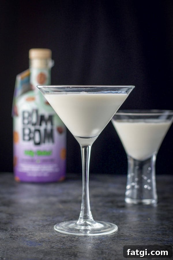 vertical view of the classic martini glass filled with the cream drink with another glass and bottle in the background