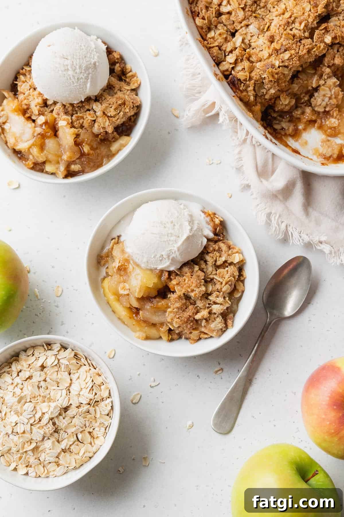 Homemade Gluten-Free Apple Crisp Recipe 4 Two bowls of gluten free apple crisp with vanilla ice cream, and a baking dish of more apple crisp placed nearby.
