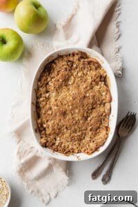 Homemade Gluten-Free Apple Crisp Recipe 9 Baked apple crisp on a beige linen with a spoon, fork, and some green apples placed next to it.