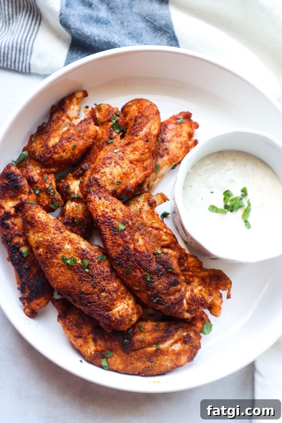 white bowl with blackened chicken tenders with a side of ranch topped with green onion.