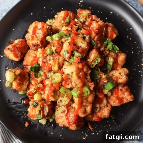black plate with salt and pepper tofu topped with green onion, red chili pepper, and garlic