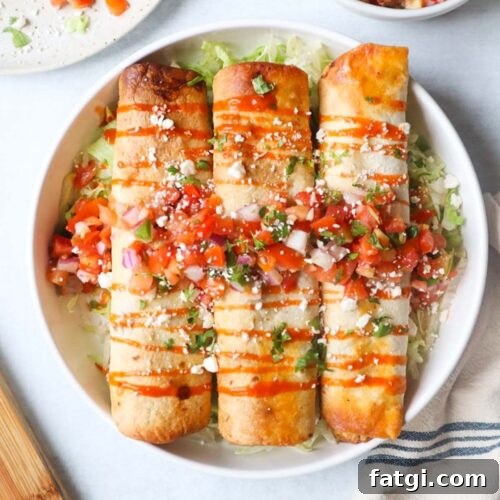 white plate with three chicken flautas on top of a bed of lettuce, topped with hot sauce, pico de gallo, and cotija cheese