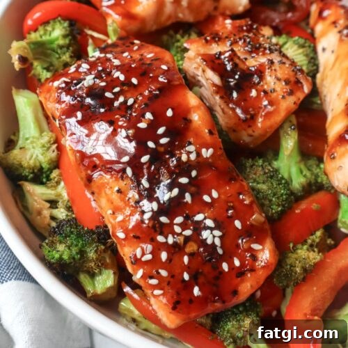 white plate with red bell pepper, broccoli, cooked salmon topped with sauce and sesame seeds