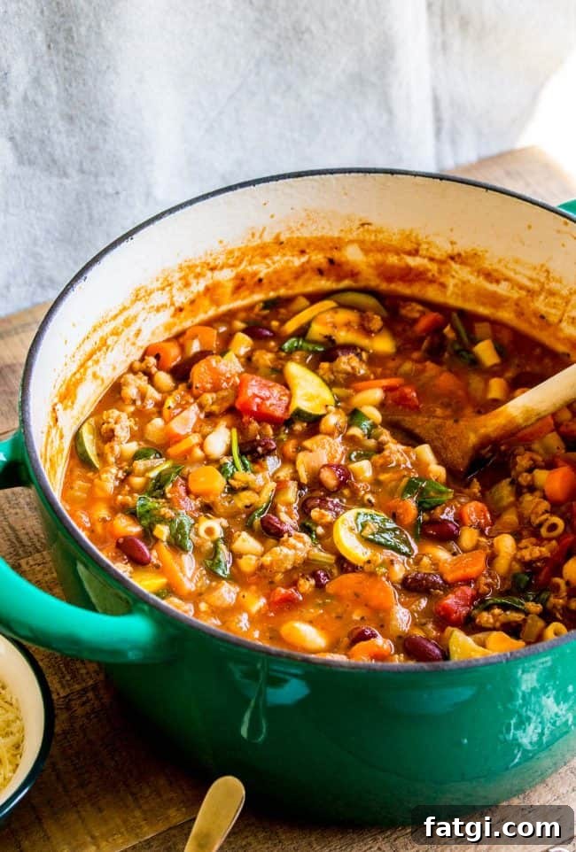 minestrone soup with sausage in a pot with a wooden spoon.