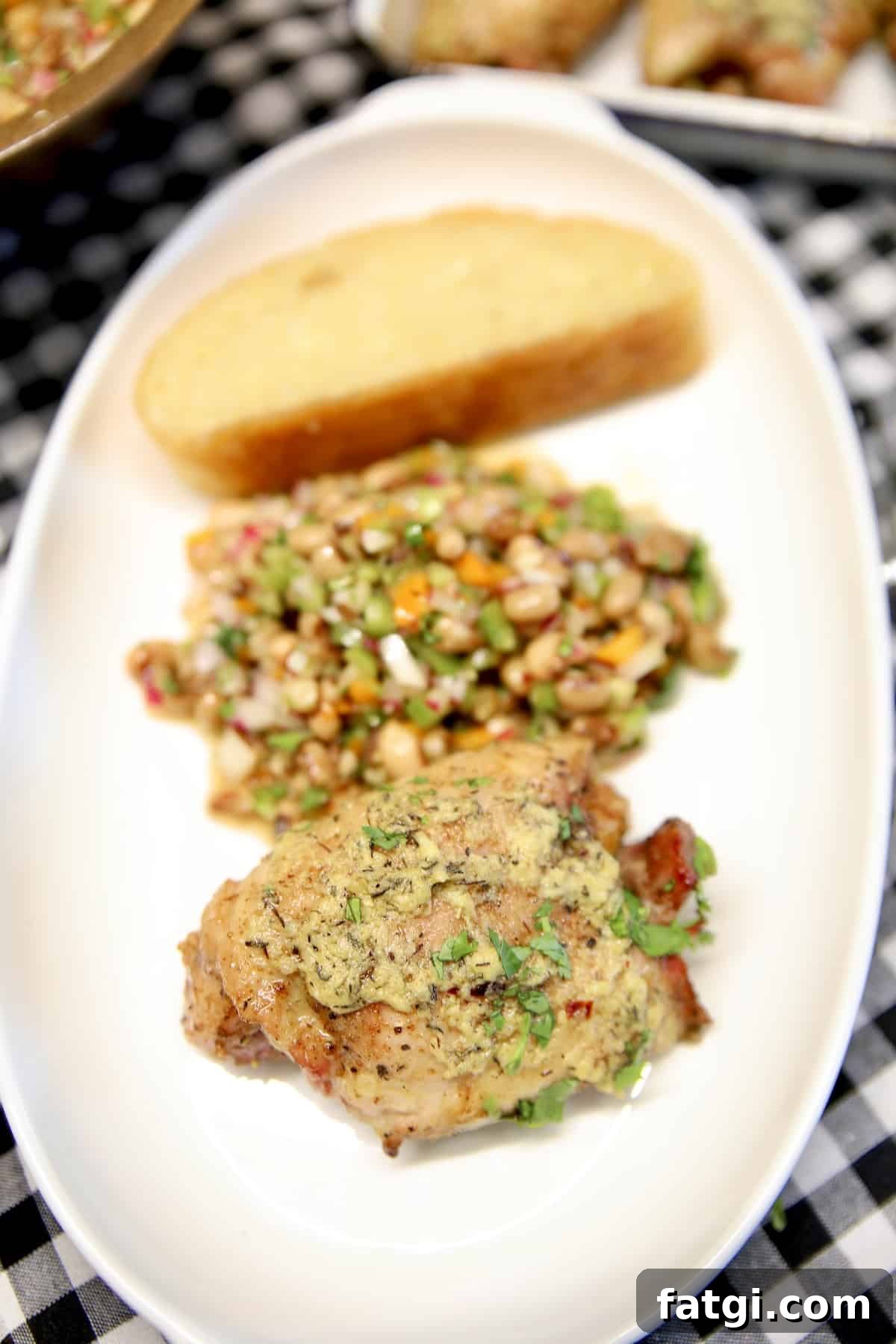 Garlic butter chicken thigh, black eyed pea salad and bread on a platter.