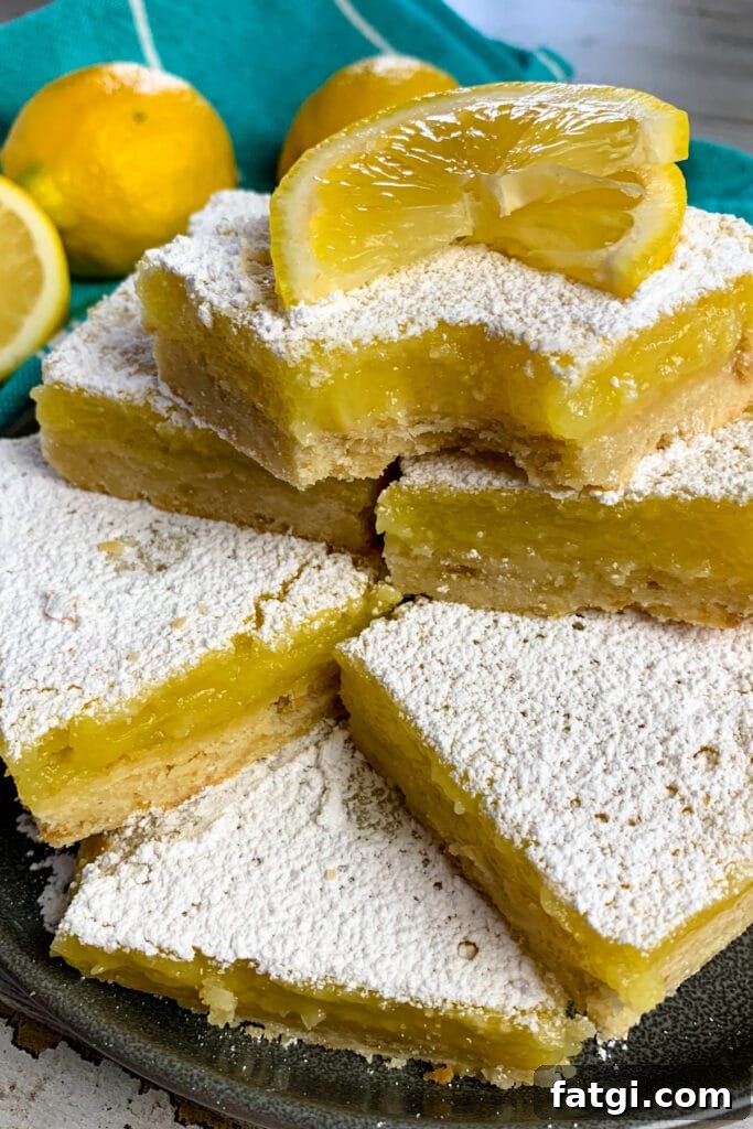 Lemon bars are stacked up on a plate and garnished with a sliced lemon.