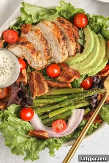 Salad bowl filled with a BLT salad with chicken, avocado, asparagus, and a side of ranch.