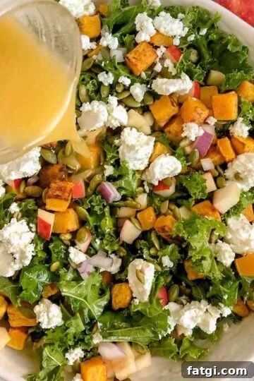 Dressing being poured on kale salad with butternut squash.