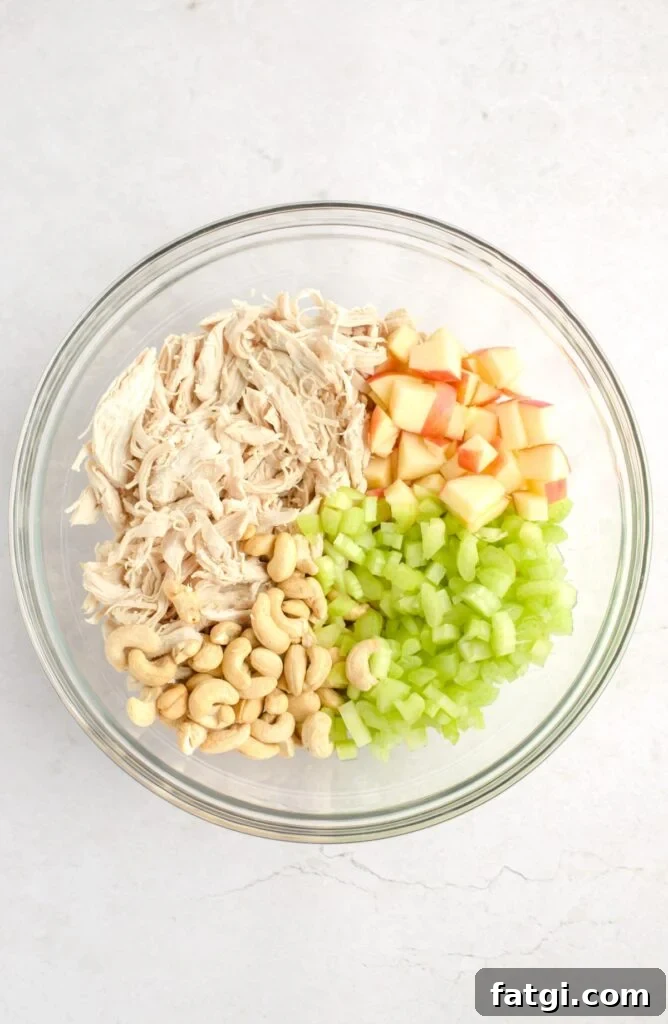 Shredded chicken, diced apples, diced celery, and cashews in a mixing bowl.