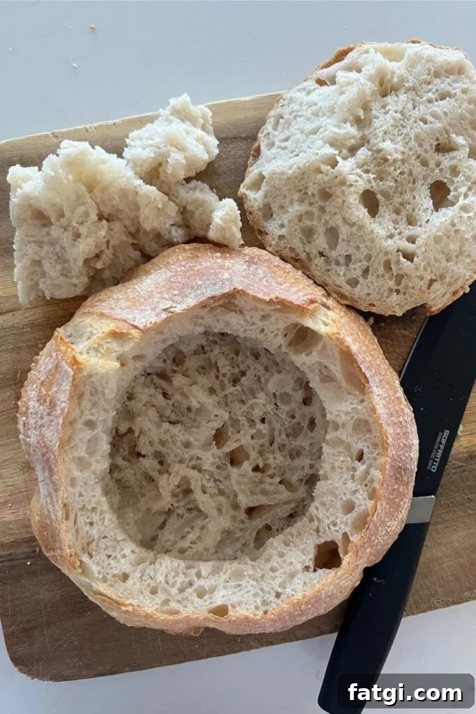 A sourdough bread bowl that has been hollowed out. There is a sharp, black knife sitting to the right of the bread bowl.