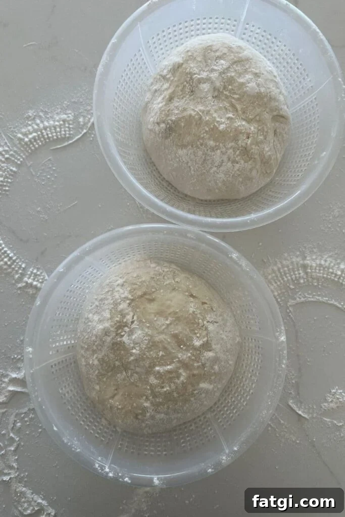 Two plastic ricotta baskets holding a loaf of sourdough each. There is a lot of rice flour sprinkled around them.