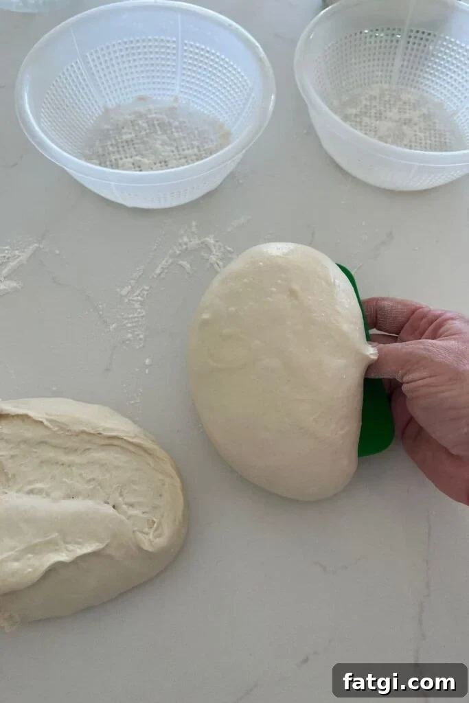 Two ricotta baskets sitting in the background with two dough balls being lifted by a green plastic dough scraper.