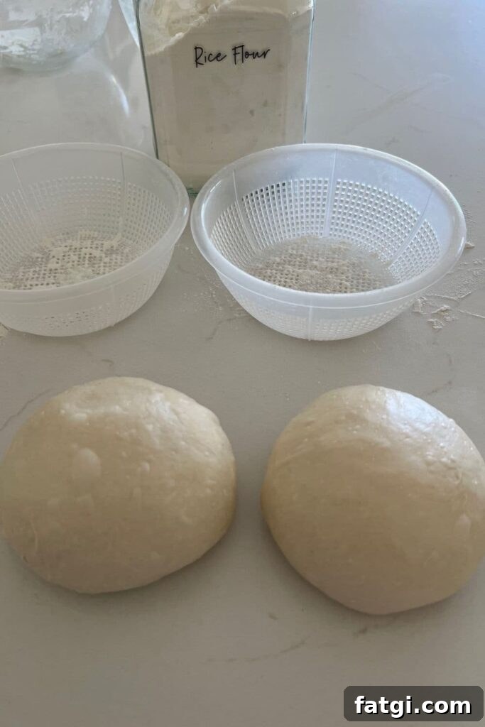 Two shaped sourdough bread bowls sitting in front of two plastic ricotta baskets. There is a glass jar of rice flour in the background.
