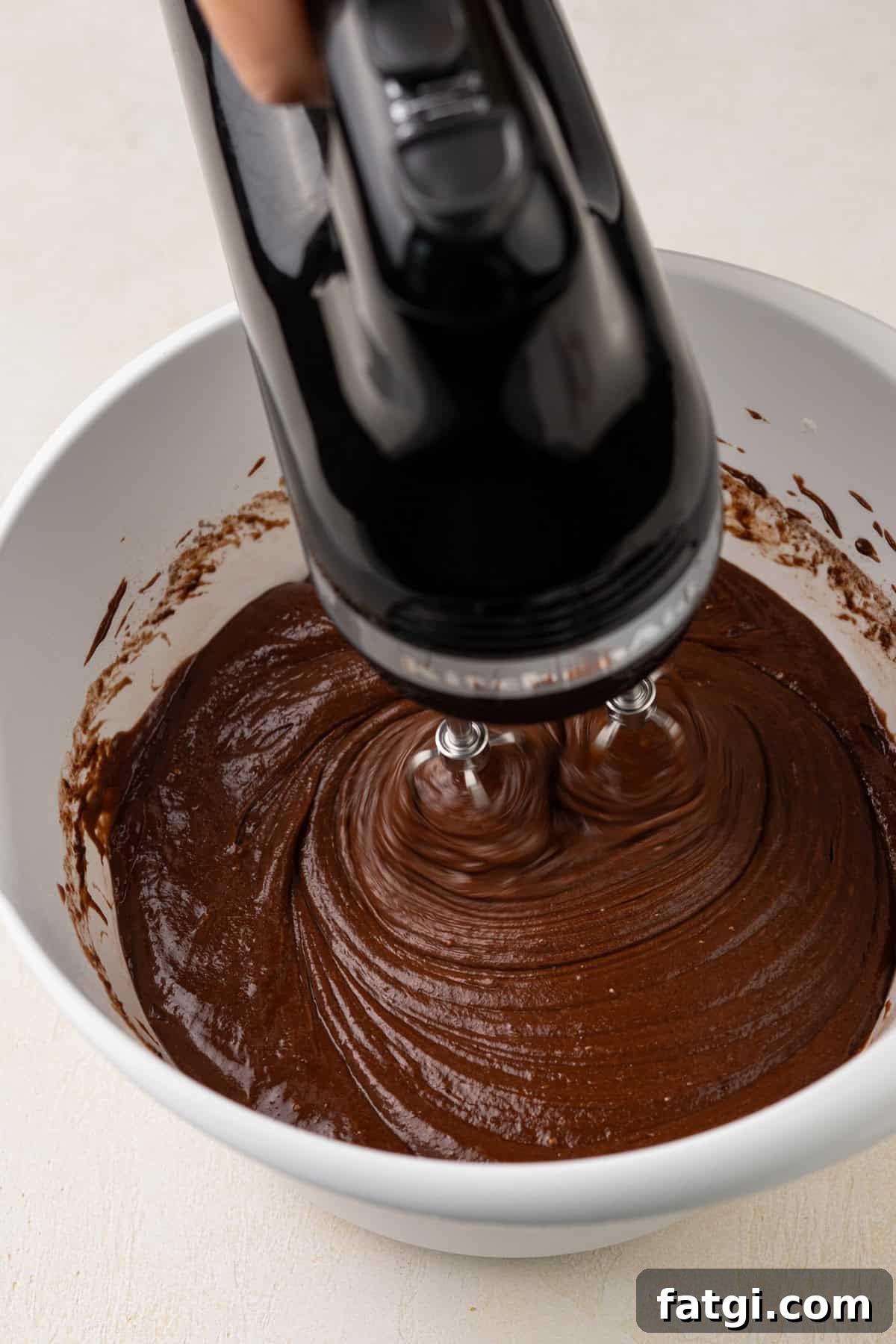 How to Transform Boxed Cake Mix into Gourmet Cakes 6 Hand mixer mixing doctored cake mix batter in a white bowl.