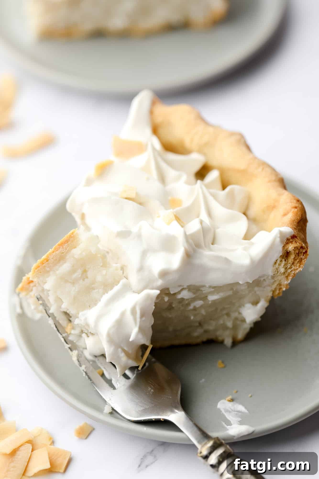a fork taking a bite out of a slice of vegan coconut cream pie on a plate.