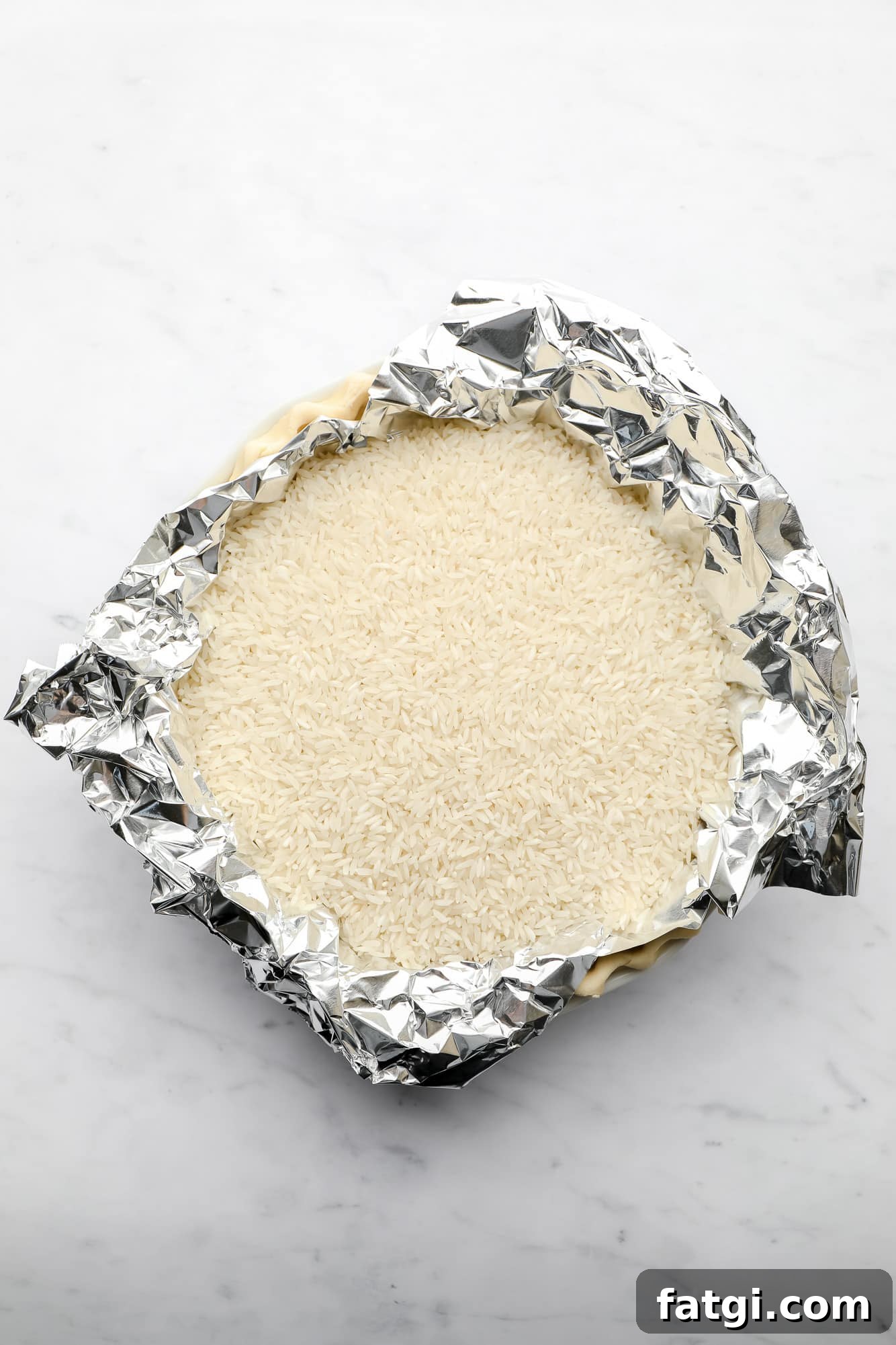 pie crust being baked in a pie plate with a layer of tinfoil and white rice on top.