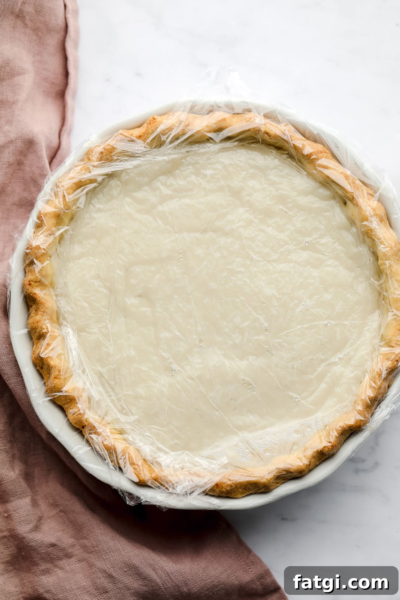 coconut custard in a pie covered with a layer of plastic wrap.