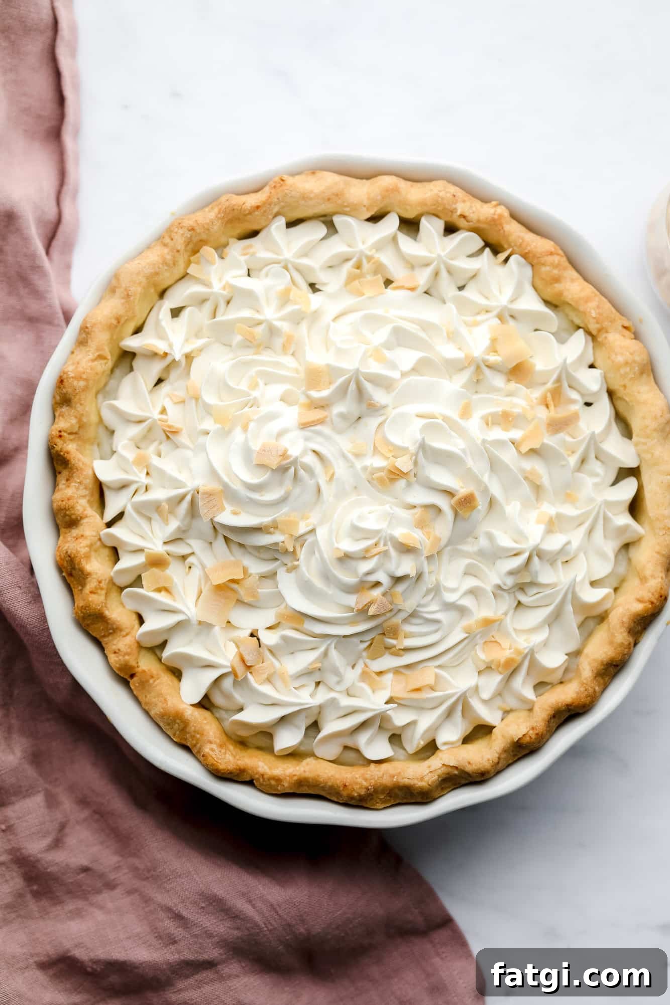 baked vegan coconut cream pie with whipped cream and toasted coconut shreds on top.