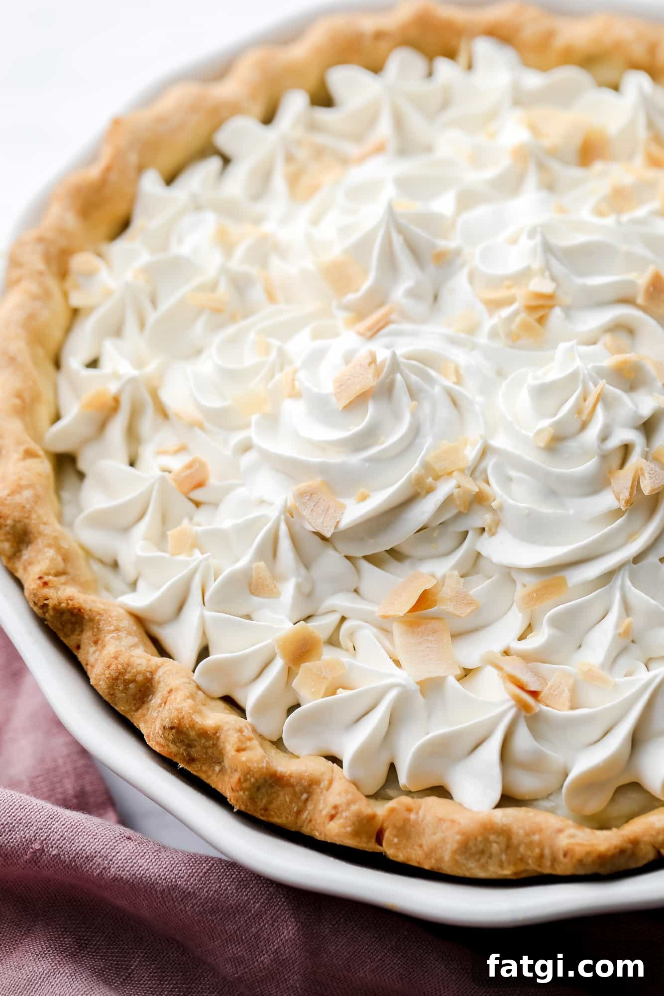 close up on a vegan coconut cream pie with whipped cream and coconut shreds on top.