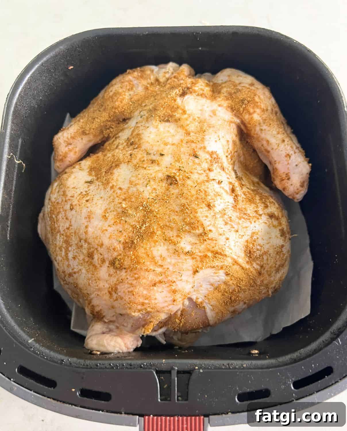 Seasoned whole chicken in air fryer basket.