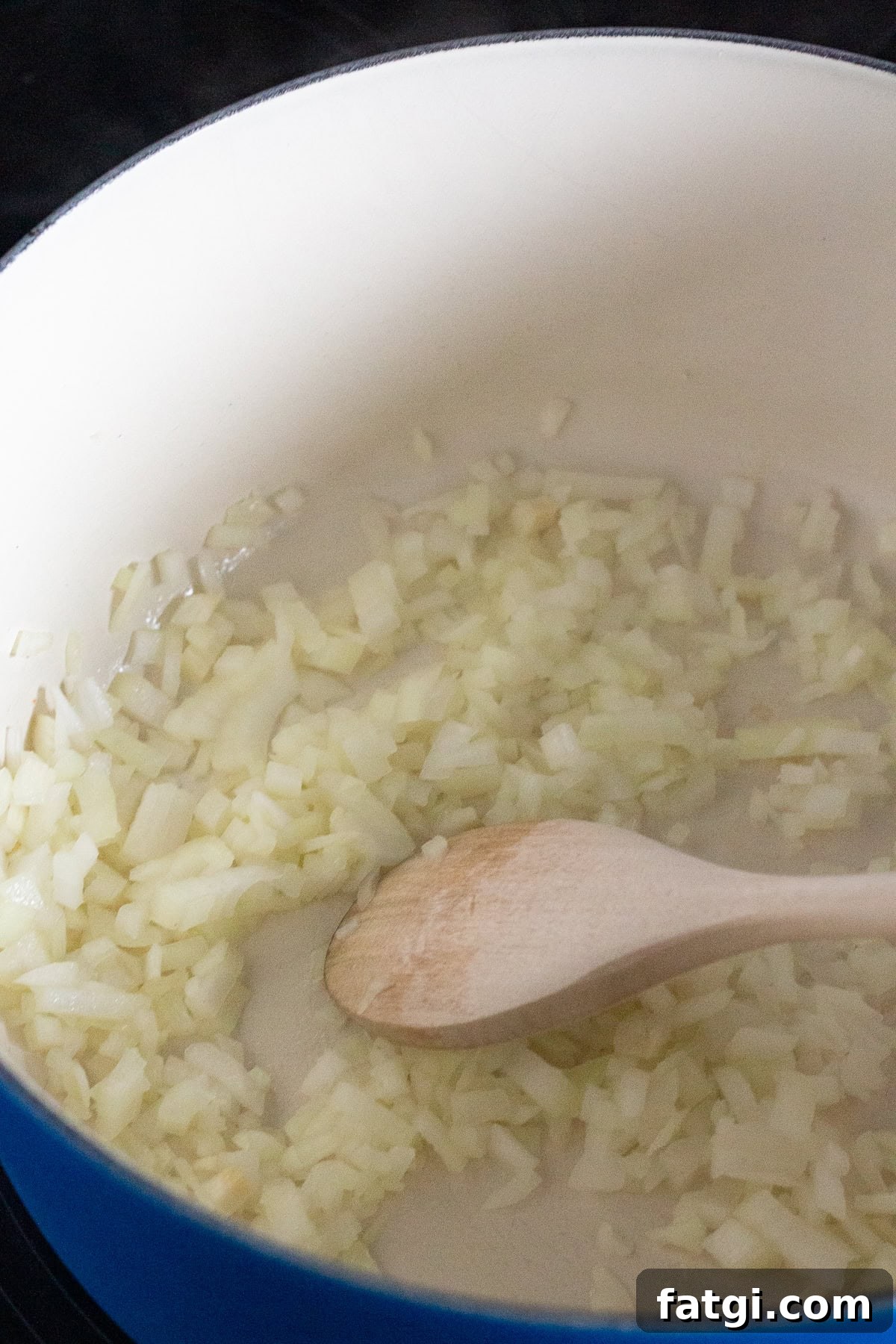Chopped onions being sautéed in a blue pot with a wooden spoon.