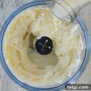 Creamy Homemade Garlic and Herb Cheese Spread Recipe 5 Milk being poured into food processor containing cream cheese.